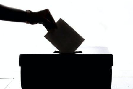 Silhouette of hand casting voting ballot into ballot box
